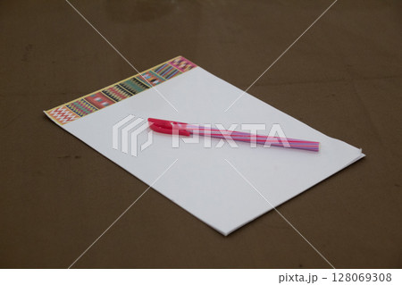 Blank white paper sheet with colorful patterned border and pen on brown surface 128069308