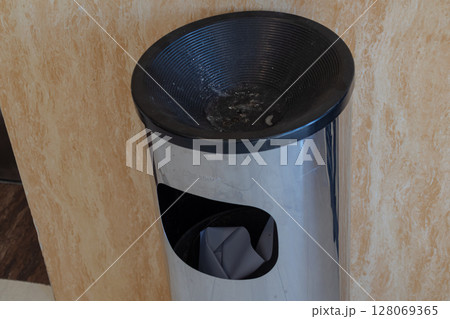 Modern stainless steel trash can with integrated cigarette ashtray in a public indoor space Modern stainless steel trash can with integrated cigarette ashtray in a public indoor space 128069365