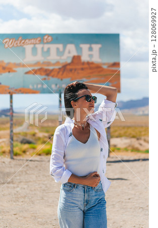 Beautiful woman on her trip by the car. Welcome to Utah road sign. Large welcome sign greets travels in Monument Valley, Utah Beautiful woman on her trip by the car. Welcome to Utah road sign. Large welcome sign greets travels in Monument Valley, Utah 128069927