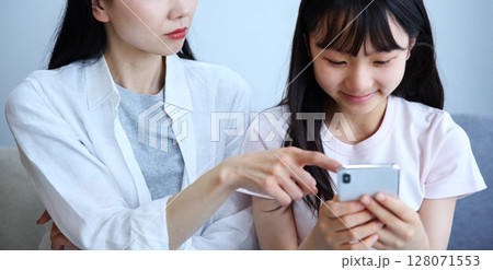 スマホに夢中になる娘に注意する母親のイメージ スマホに夢中になる娘に注意する母親のイメージ 128071553