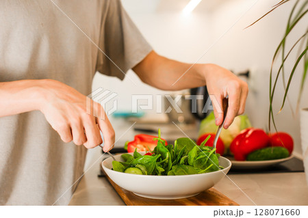 A guy is mixing while preparing a vegetarian vegetable salad with lettuce and fresh vegetables A guy is mixing while preparing a vegetarian vegetable salad with lettuce and fresh vegetables 128071660