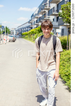 Cheerful cute teenage boy with a backpack walking down the street in sweatpants and a T-shirt 128071680