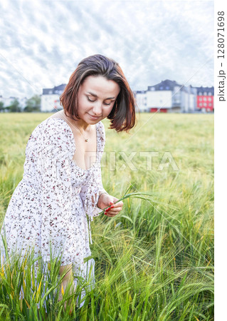 Young female agronomist collects and examines green ears of barley in a field outside the city 128071698