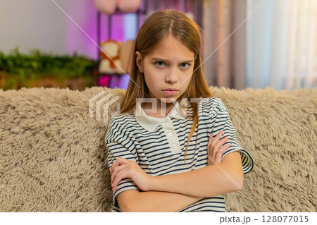 Child girl kid crosses arms in anger sitting on sofa, expressing frustration dissatisfaction at home 128077015