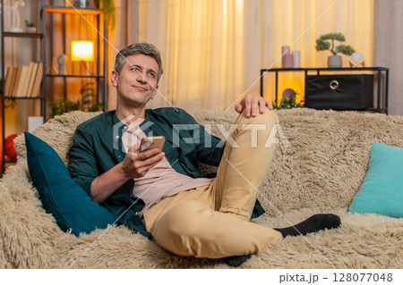 Young man smiles while browsing old family photos on smartphone, enjoying warm nostalgic moment Young man smiles while browsing old family photos on smartphone, enjoying warm nostalgic moment 128077048