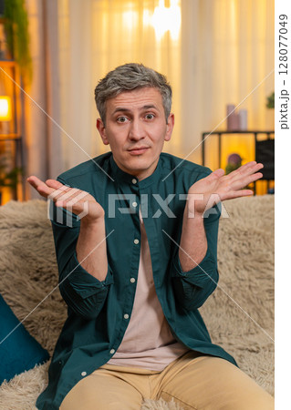 Young man lifts hands in air and looks confused reacting to unexpected situation or sudden question Young man lifts hands in air and looks confused reacting to unexpected situation or sudden question 128077049