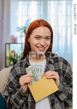 Woman sitting on sofa counting cash dollars putting part into envelope looking happy and satisfied Woman sitting on sofa counting cash dollars putting part into envelope looking happy and satisfied 128077078