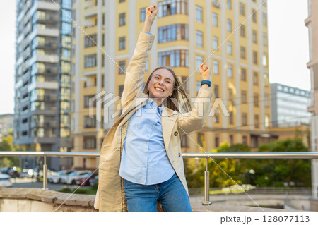 Excited woman looking surprised clenching fists, shocked by sudden victory standing on city street Excited woman looking surprised clenching fists, shocked by sudden victory standing on city street 128077113