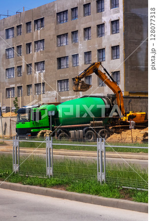 A large green concrete mixer truck is being loaded with fresh concrete 128077318