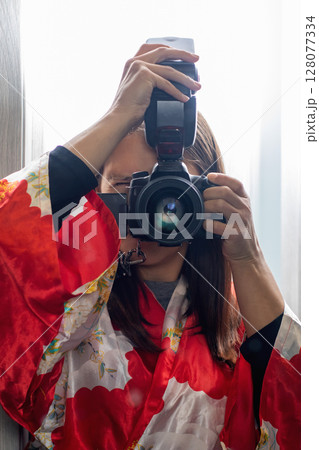 A woman in a red kimono is taking a selfie with a camera 128077334