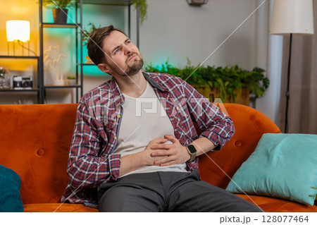 Man sits on sofa feeling sudden strong abdominal stomach ache gastritis problem poisoning diarrhea 128077464