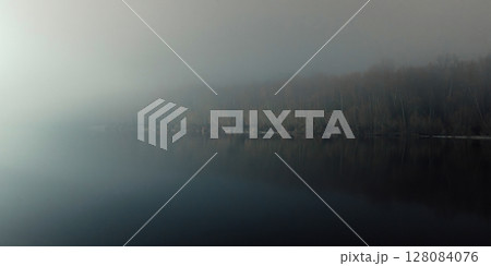 A foggy riverside at night, illuminated by distant lights, with a calm water surface and a dark 128084076