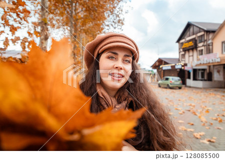 Fall elegance captured in motion as a young woman strolls through quiet city corners, enjoying the peaceful vibe of her weekend break. Bouquet of orange leaves in close-up Fall elegance captured in motion as a young woman strolls through quiet city corners, enjoying the peaceful vibe of her weekend break. Bouquet of orange leaves in close-up 128085500
