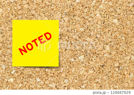 Yellow note paper with word noted on cork board background with copy space 128087029
