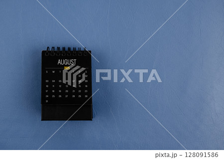 August 2025 black desk calendar on navy blue color leather background. 128091586