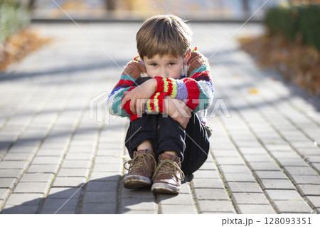 Sad little boy sits on the alley in the park. The child put his head on his knee. 128093351