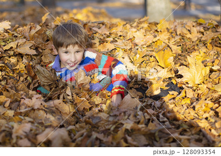 Happy little boy in a pile of yellow leaves in the autumn park. Happy little boy in a pile of yellow leaves in the autumn park. 128093354