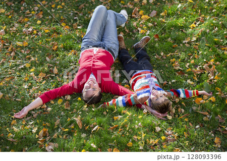 Mom and little one lie on the grass in the autumn park. Mom and little one lie on the grass in the autumn park. 128093396