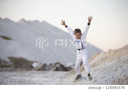 Young boy in a suit of an American astronaut jumps against a background of white mountains. Young boy in a suit of an American astronaut jumps against a background of white mountains. 128093576