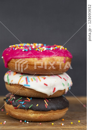 Lovely sweet food. Stack of glazed colorful assorted donuts with splashes on a gray background. 128093652