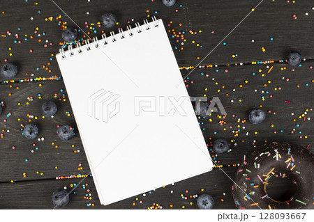 On a wooden background, a blank notebook, chocolate donuts and blueberries. Creative cuisine. On a wooden background, a blank notebook, chocolate donuts and blueberries. Creative cuisine. 128093667