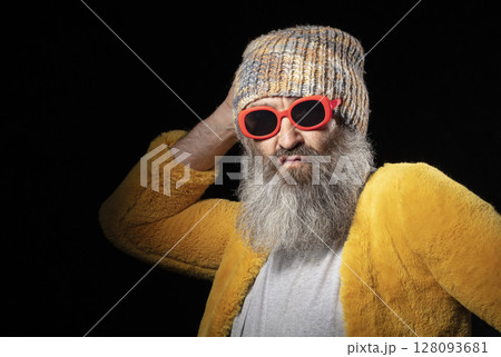 Creative elderly man with a gray beard in fashionable clothes on a black background. Creative elderly man with a gray beard in fashionable clothes on a black background. 128093681