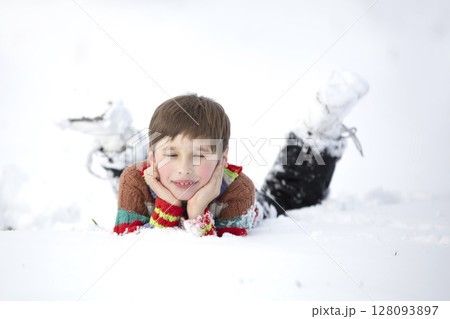 A funny little boy in colorful clothes lies in the snow. A hardened child in winter. 128093897