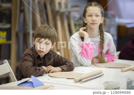 A girl and a boy are sitting at a desk in a clay modeling lesson. 128094080