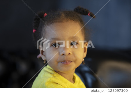 Little African American girl of two years old with pigtails looks at the camera. 128097300