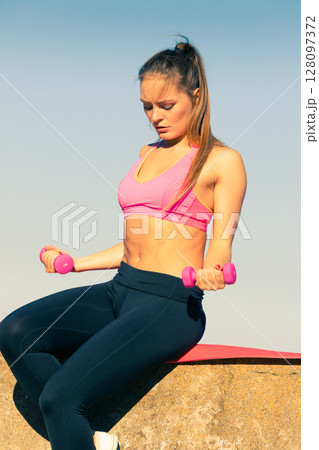 Woman doing sports outdoors with dumbbells Woman doing sports outdoors with dumbbells 128097372