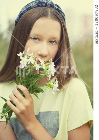 A teenage girl with creative makeup holds a bunch of wildflowers in her hands. Cute girl with long hair in the meadow. A teenage girl with creative makeup holds a bunch of wildflowers in her hands. Cute girl with long hair in the meadow. 128097832