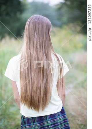 A girl with long white hair from behind against a background of a green meadow. 128097836