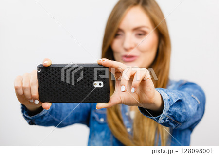 Woman in denim shirt taking self picture with phone 128098001