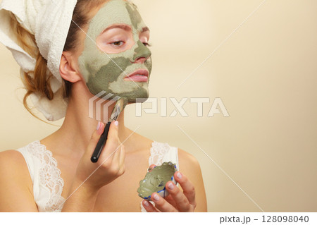 Woman applying with brush clay mud mask to her face Woman applying with brush clay mud mask to her face 128098040