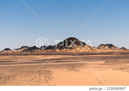 Ash-covered hills in Egypt's Black Desert under a clear sky, scenic and remote landscape. Volcanic Ash-covered hills in Egypt's Black Desert under a clear sky, scenic and remote landscape. Volcanic 128098997