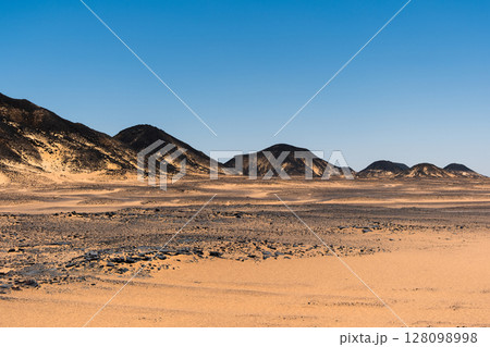 Ash-covered hills in Egypt's Black Desert under a clear sky, scenic and remote landscape. Volcanic Ash-covered hills in Egypt's Black Desert under a clear sky, scenic and remote landscape. Volcanic 128098998