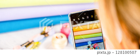 A woman takes a photo on a smartphone. Accessories for hobby embroidery knitting 128100507