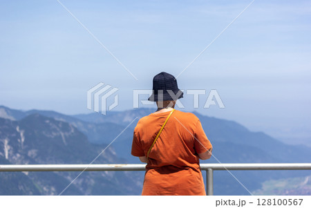 A solo traveler looks at the Bavarian Alps in sunny summer weather 128100567