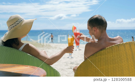 Couple clinks glasses with fruit shakes on tropical beach during vacation Couple clinks glasses with fruit shakes on tropical beach during vacation 128100588