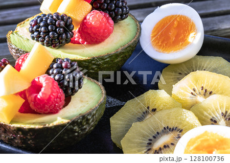 Vibrant healthy food with blackberry, redberry and mango on avocado with golden kiwi and boiled egg is eating colorful on ceramic dish. 128100736