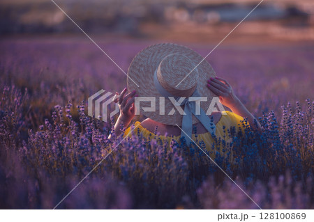 Lavender Woman Hat: Back view in field at sunset, holding flowers, serene moment. Lavender Woman Hat: Back view in field at sunset, holding flowers, serene moment. 128100869