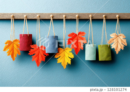 Small textile gift bags and bright autumn leaves hanging on wooden hooks against a blue wall 128101274