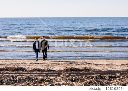 Loving couple walks on beach along sea on sunny autumn day. Weekend and lifestyle concept. High quality photo Loving couple walks on beach along sea on sunny autumn day. Weekend and lifestyle concept. High quality photo 128102034