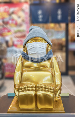 [大阪・天神橋] ニット帽、マフラー、フェイスマスクをつけた金色のビリケンの彫刻。 128102548
