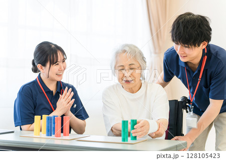 介護施設・リハビリ施設で働く作業療法士の職員とリハビリをするシニア女性 128105423