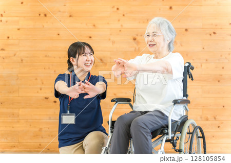 リハビリで体操をする車椅子に乗ったシニア女性と理学療法士・作業療法士の女性スタッフ リハビリで体操をする車椅子に乗ったシニア女性と理学療法士・作業療法士の女性スタッフ 128105854