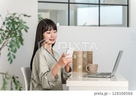 家,オフィスでスマホ,スマートフォンを使って仕事する若いアジア人女性 家,オフィスでスマホ,スマートフォンを使って仕事する若いアジア人女性 128108568