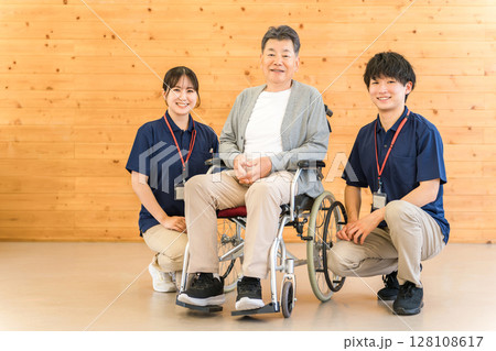 車椅子のシニア男性と介護士・ケアマネージャーの男女スタッフ（認知症・リハビリ） 128108617