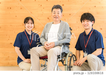 車椅子のシニア男性と介護士・ケアマネージャーの男女スタッフ(認知症・リハビリ) 車椅子のシニア男性と介護士・ケアマネージャーの男女スタッフ(認知症・リハビリ) 128108618