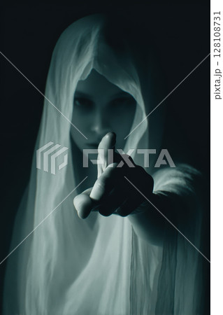 Ghostly figure in white veil points finger at viewer, mysterious and eerie atmosphere Ghostly figure in white veil points finger at viewer, mysterious and eerie atmosphere 128108731